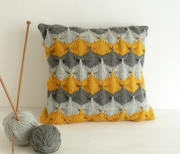 Geometric Patterned Knit Pillow Sitting Next to Knitting Needles