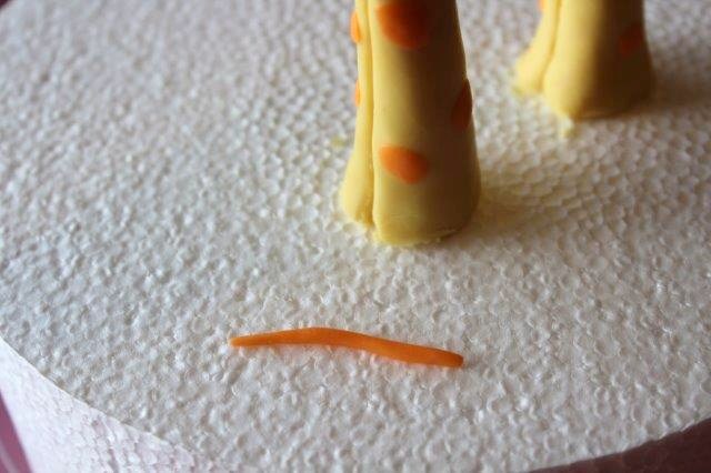 Small Rolled Orange Piece of Modeling Chocolate Next to Giraffe's Legs