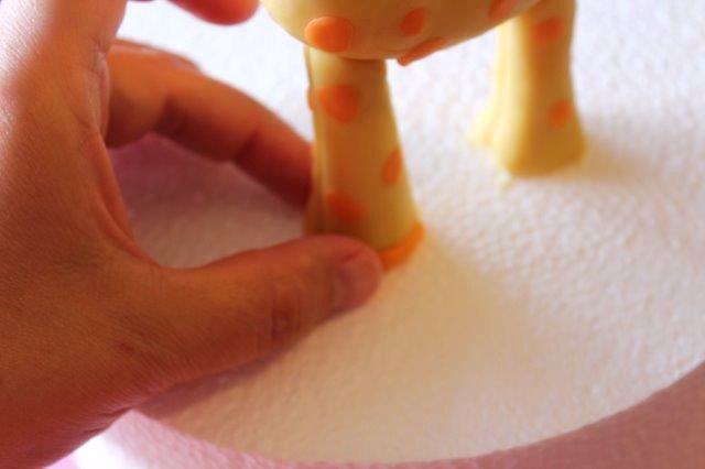 Adding Small Orange Modeling Chocolate Piece to Giraffe's Feet