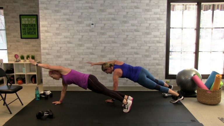 Two women working out in front of a white brick wall