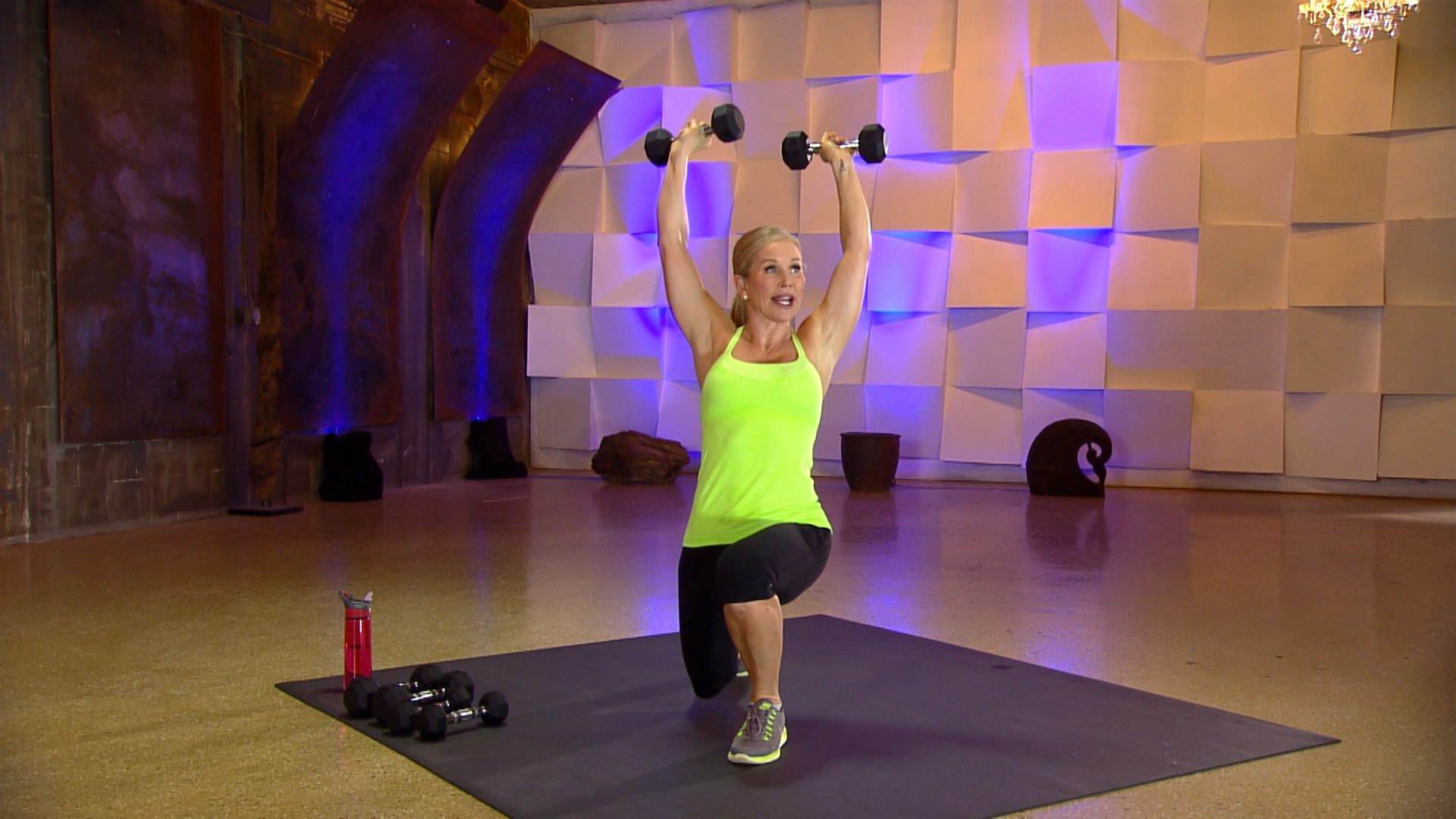 Woman in a bright tank top with dumbbells overhead