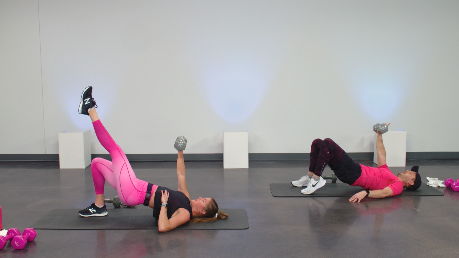 Two people wearing pink doing glute bridges with dumbbells