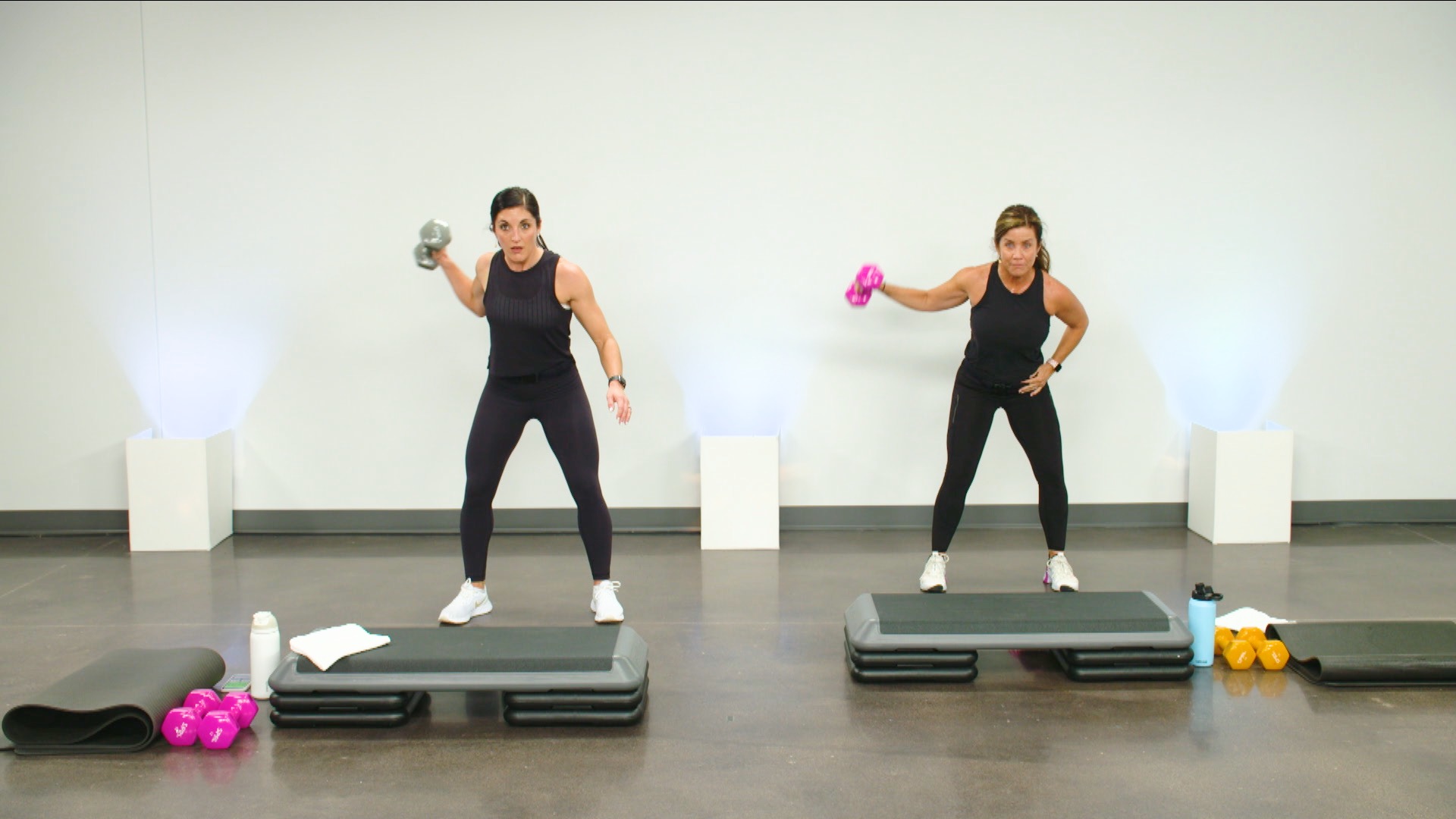 Two women working out with a dumbbell in one hand and a step