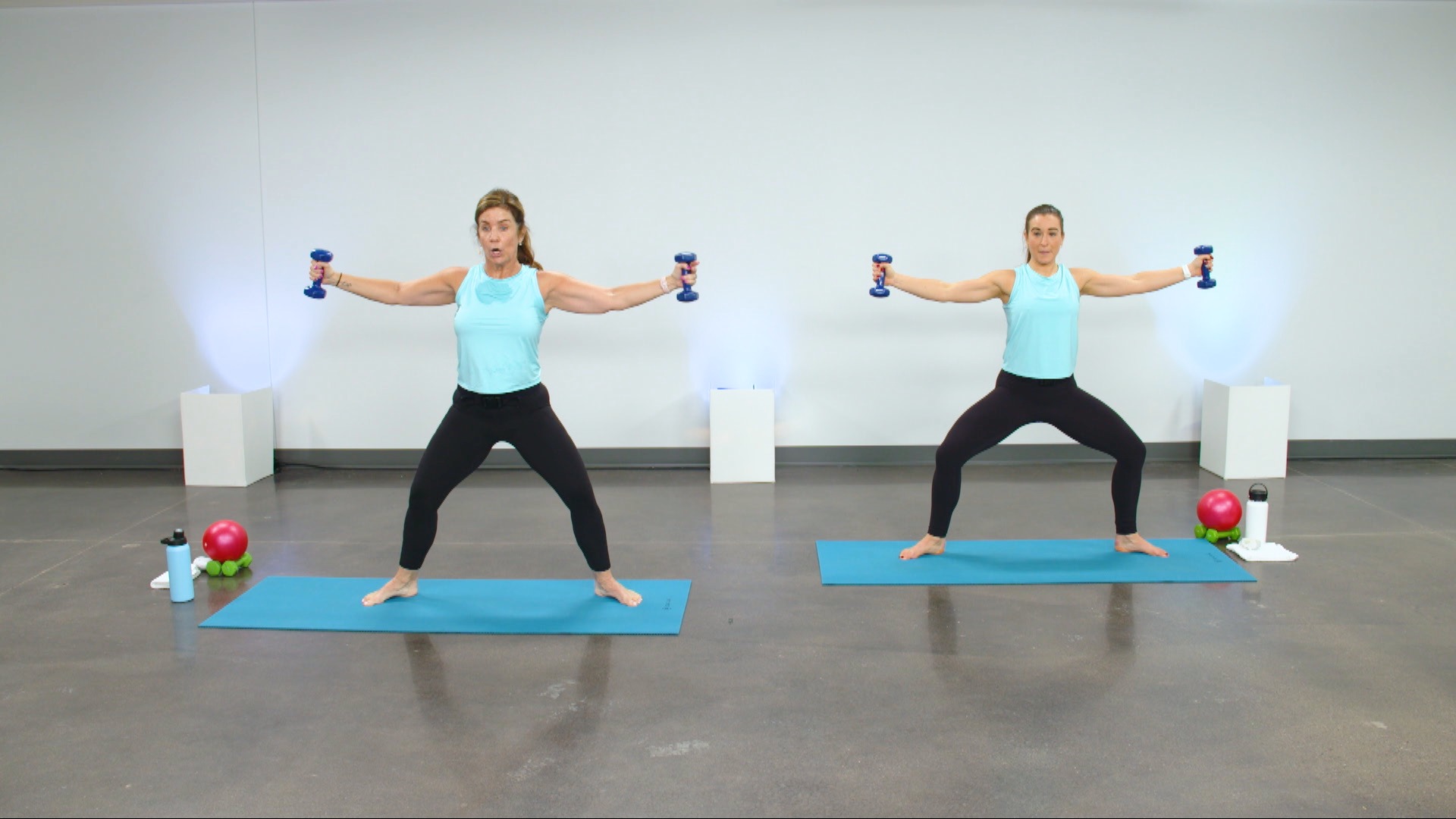 Two women doing a barre class with light weights