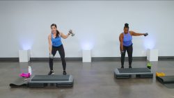 Two women in blue tank tops doing one arm lateral raises with dumbbells