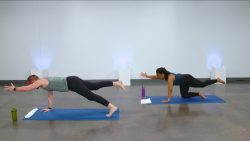 Two women doing plank reaches on blue mats