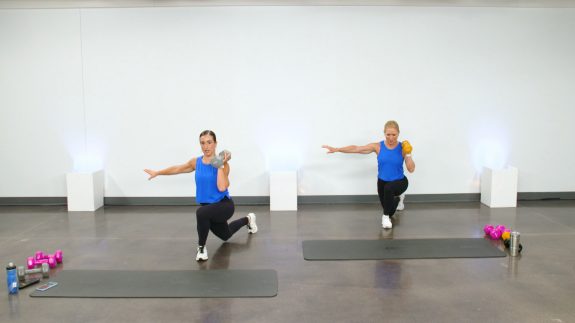 Two women doing curtsy lunges with dumbbells