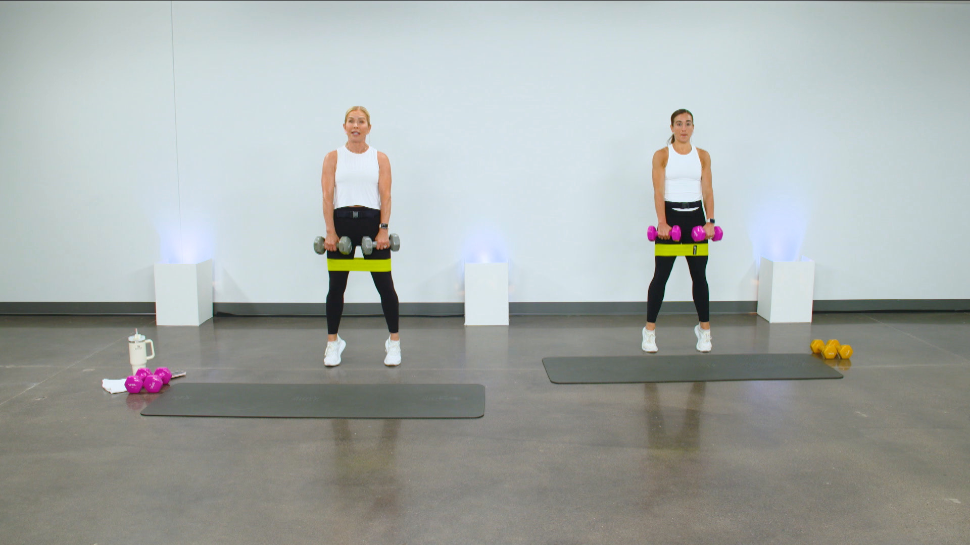 Two women doing a dumbbell workout with resistance bands on their legs