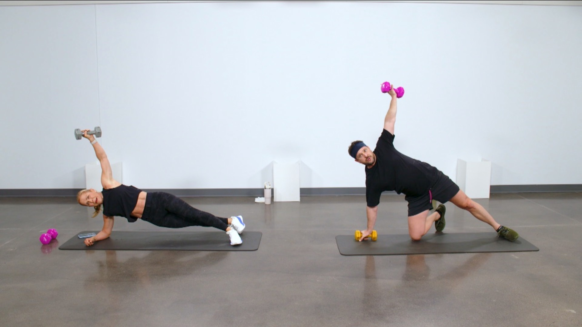 Two people holding a side plank with a dumbbell
