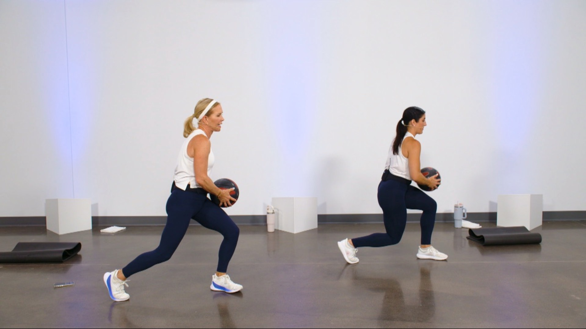 Two women doing lunges with a medicine ball
