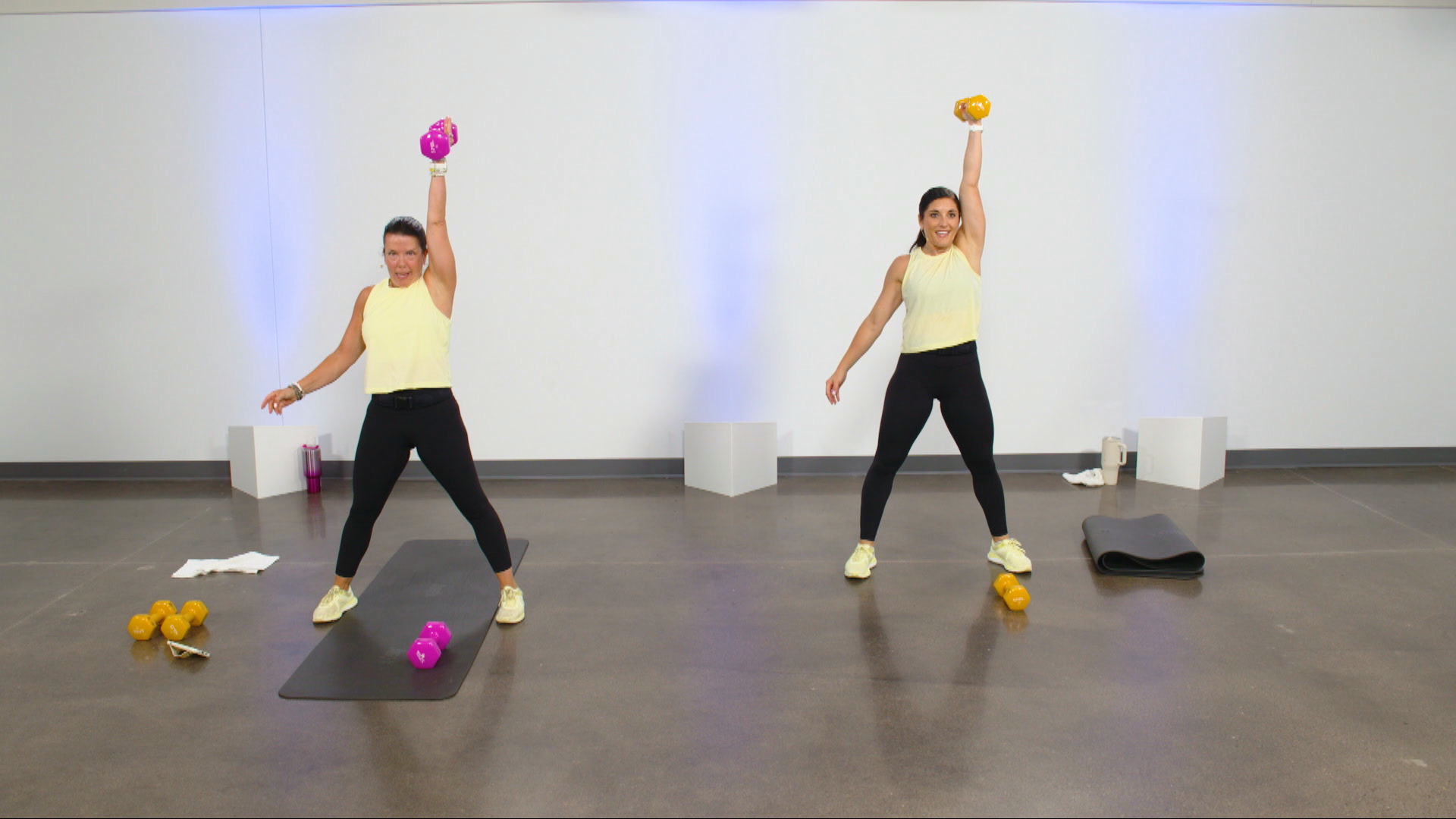 Two women in yellow tank tops doing single arm shoulder presses