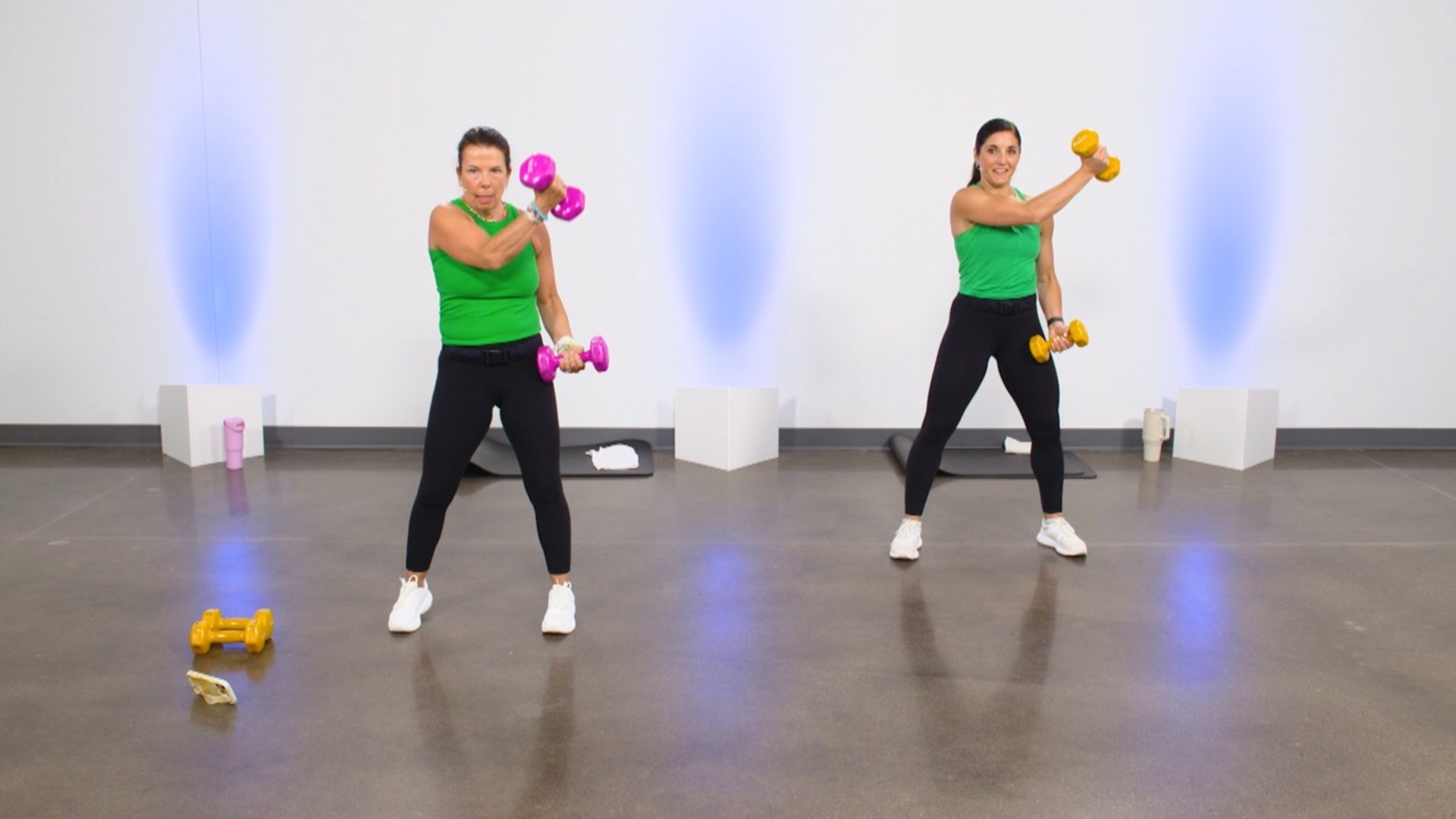 Two women in green tops working out with dumbbells