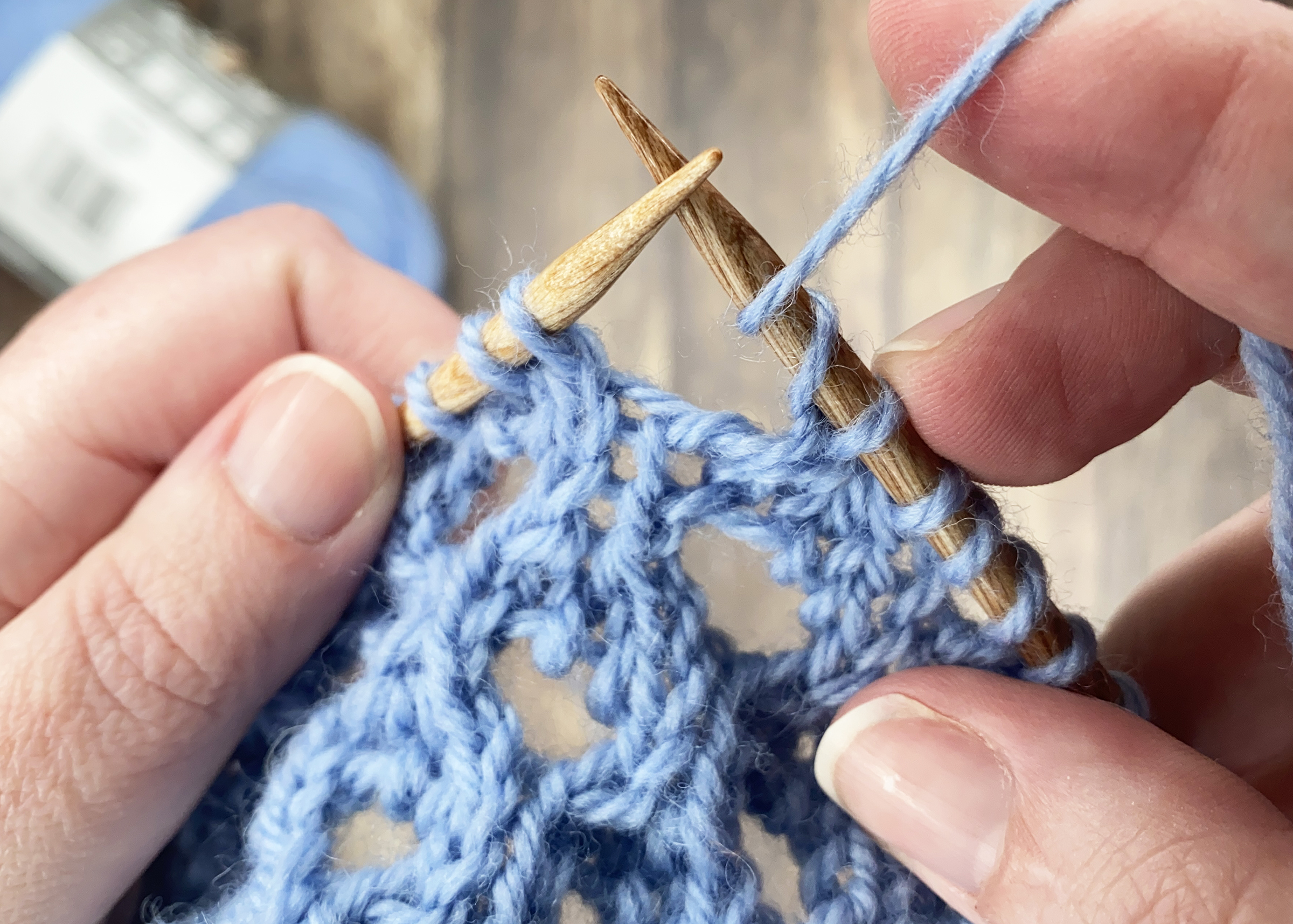 close up of knitting instructor showing a double yarn over stitch with blue yarn