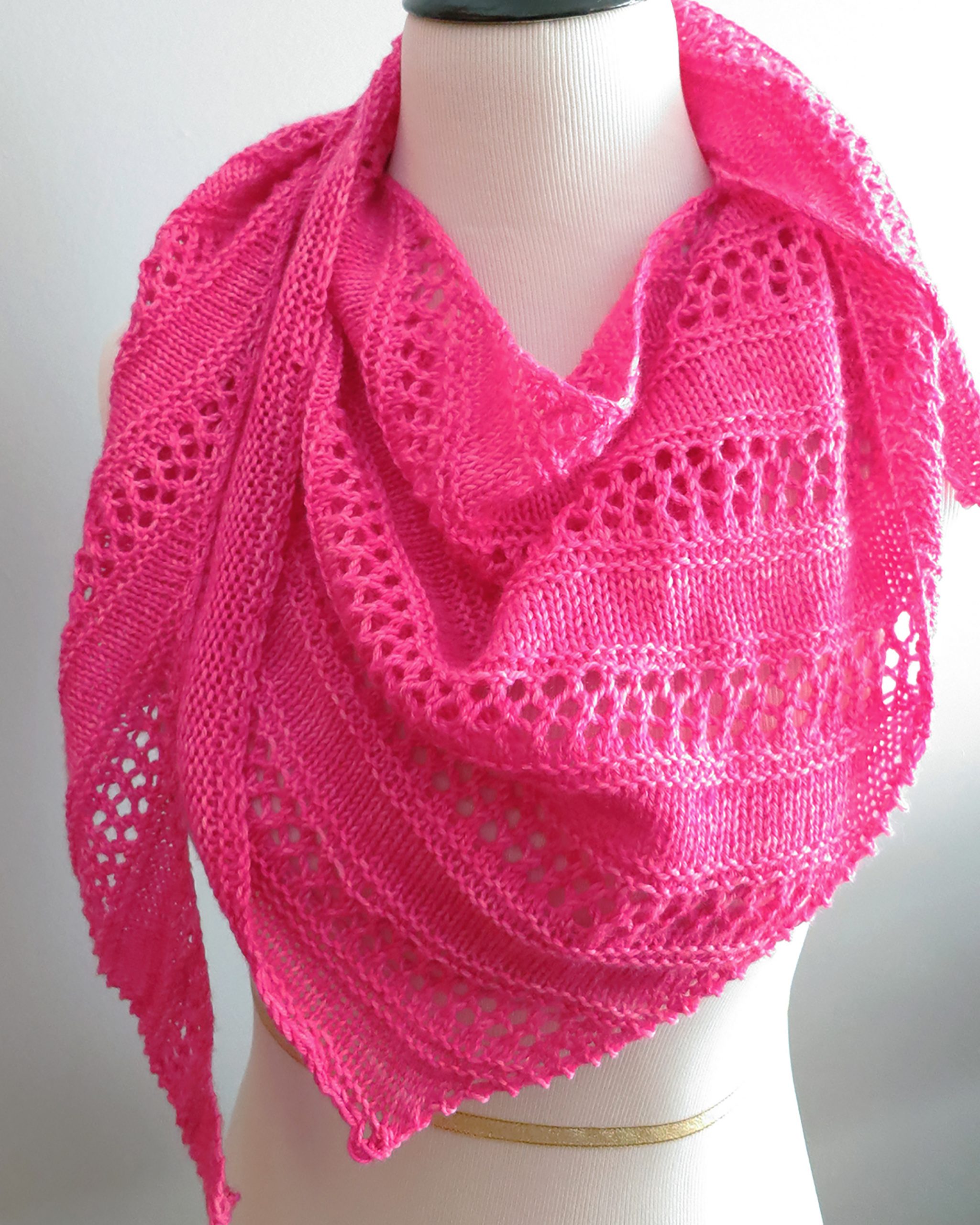 a knitted bright pink shawl displayed on a mannequin 