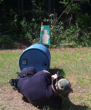 Man practicing shooting on the ground behind small object for cover