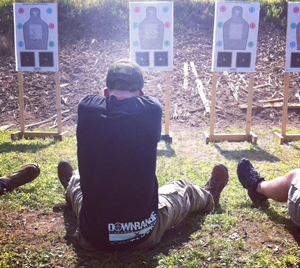 A man practicing his shooting while sitting on the ground at a target