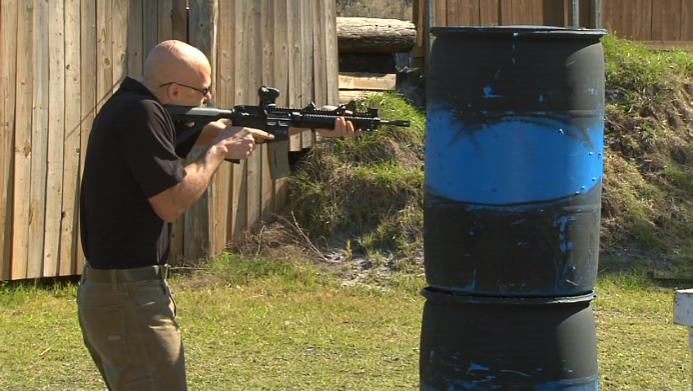 Man aiming an AR-15 around a barrel