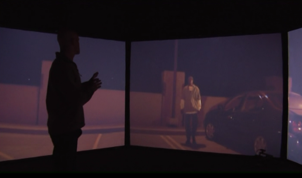Man in front of screens showing someone in a parking lot at night
