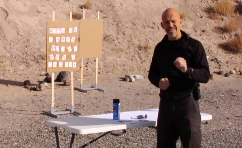 Man talking by a folding table and a gun target with playing cards