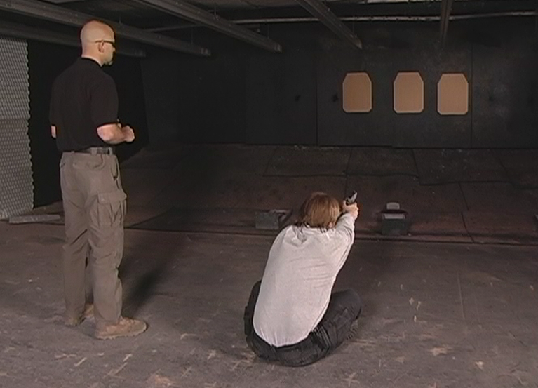 Person aiming a gun while sitting on the ground