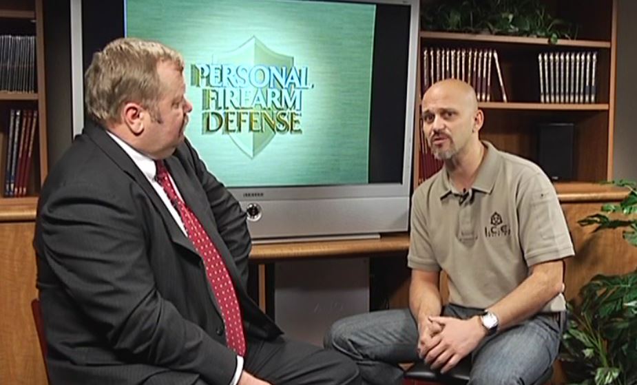 Two men talking in front of a TV with the PDN logo
