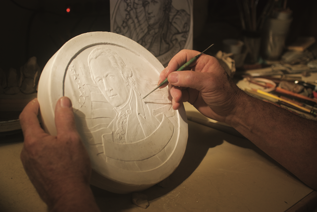 Person sculpting a large coin