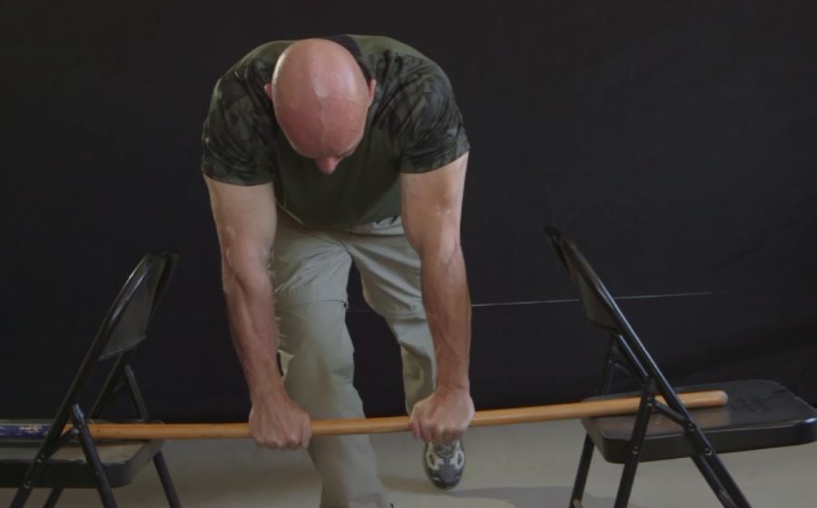 Man practicing grip strength with a rod between folding chairs