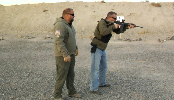 Man watching a man aim a rifle
