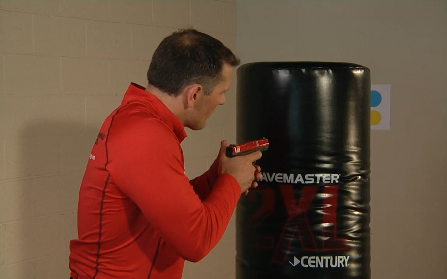 Man with a practice gun behind boxing equipment