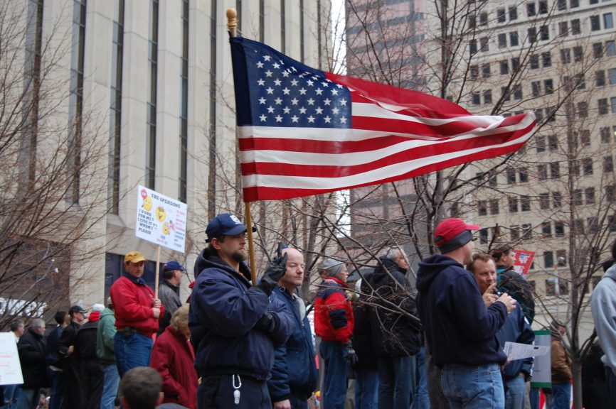 People outside with a man holding a large United States flag