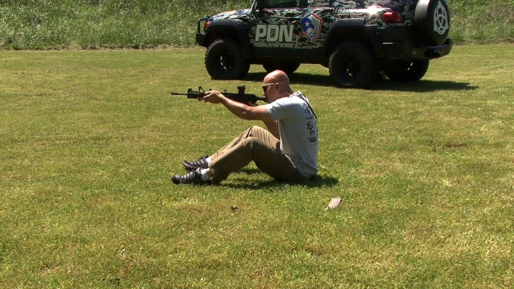 Man sitting on the ground aiming a rifle