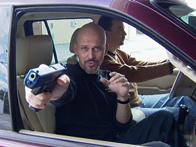 Man aiming a gun out the window of a car