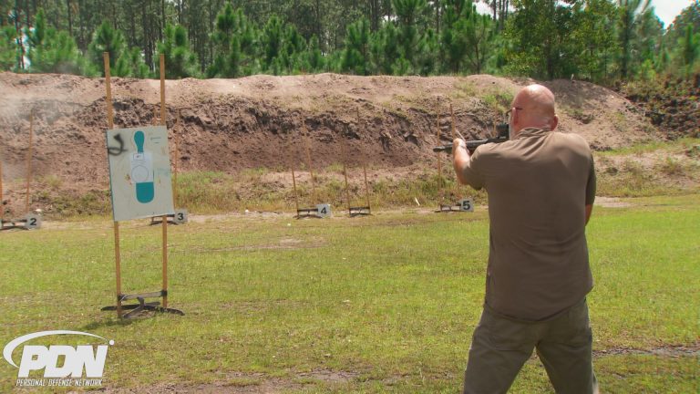 Man outside aiming a rifle at a target
