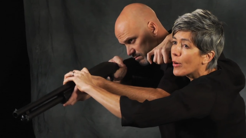 Woman with her hands on a shotgun that a man is holding