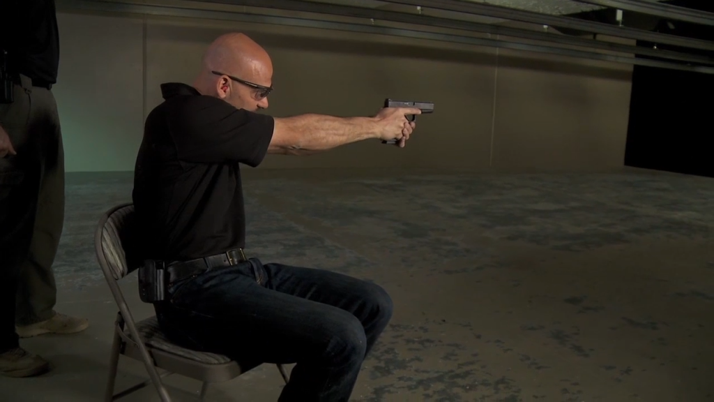 Man sitting in a chair aiming a handgun