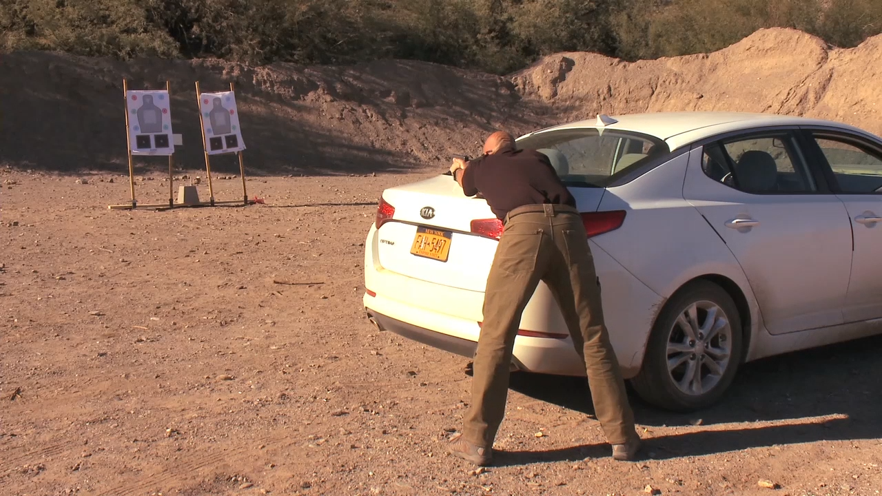 Man aiming a handgun over the trunk of a car