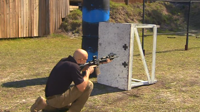 Man aiming an AR-15 around a table