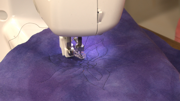 Sewing a flower on purple fabric
