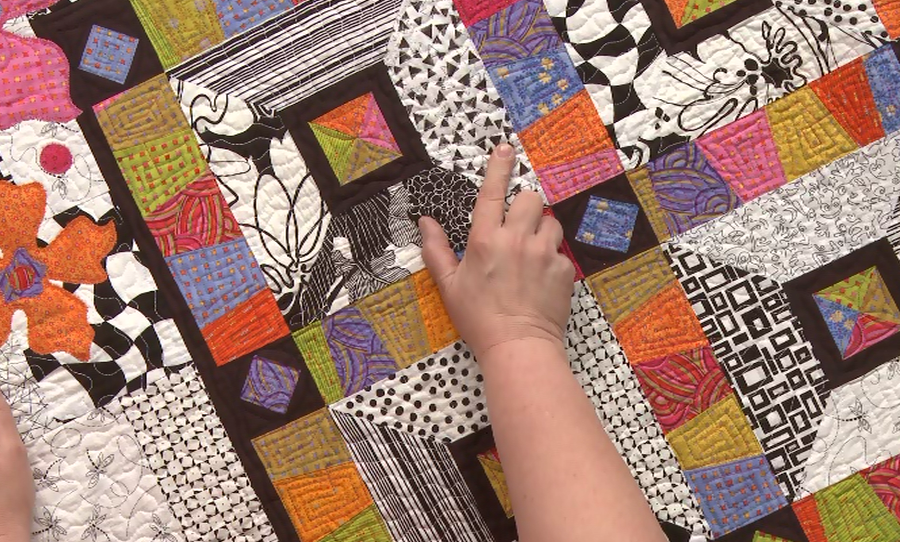 Person pointing to a colorful quilt