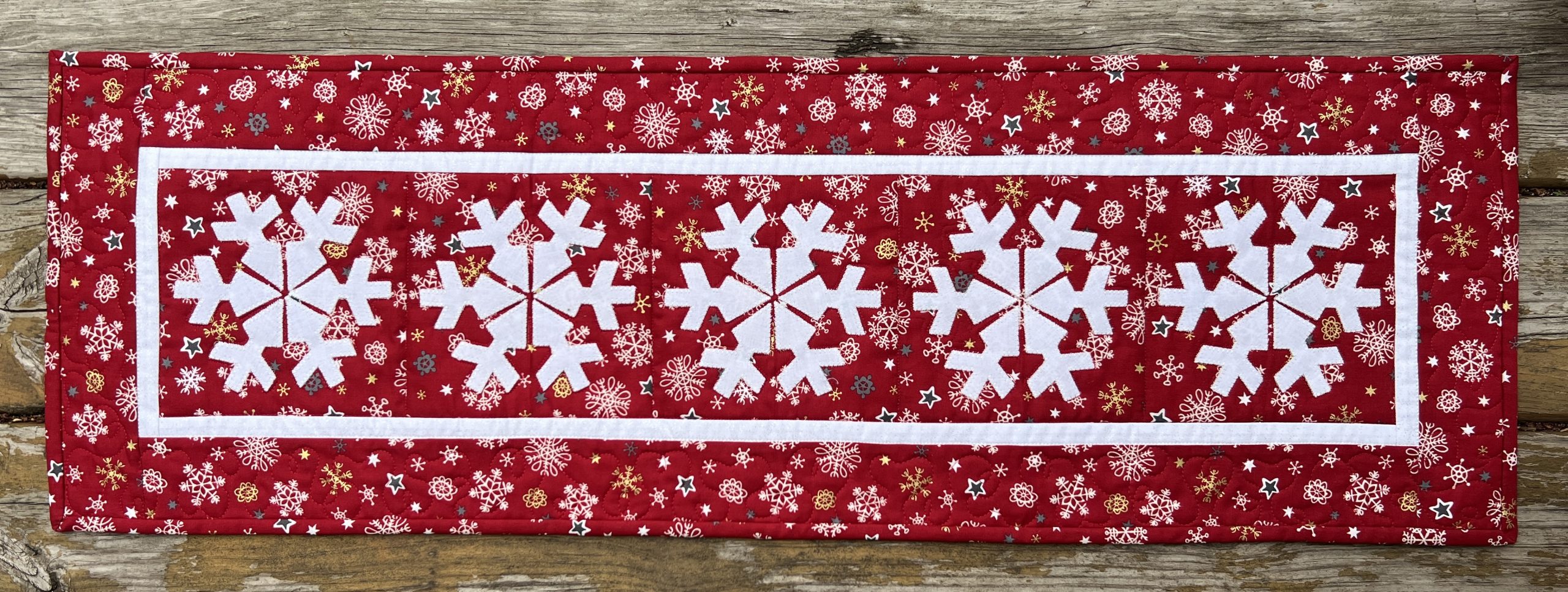 Red and white applique quilted table runner that has five snowflakes on it