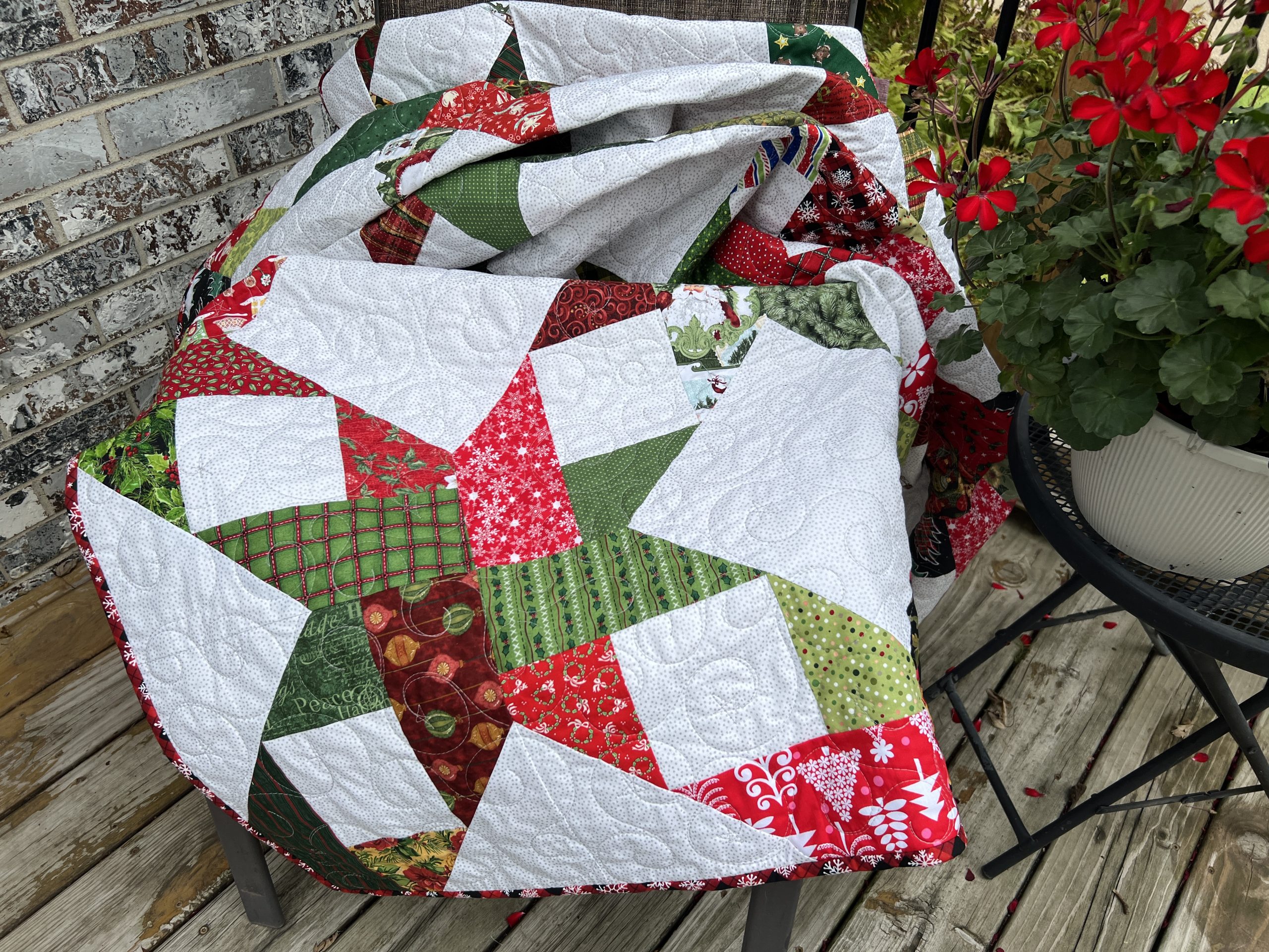 A white, green, and red christmas quilt sitting on a chair featuring a scrappy star motif