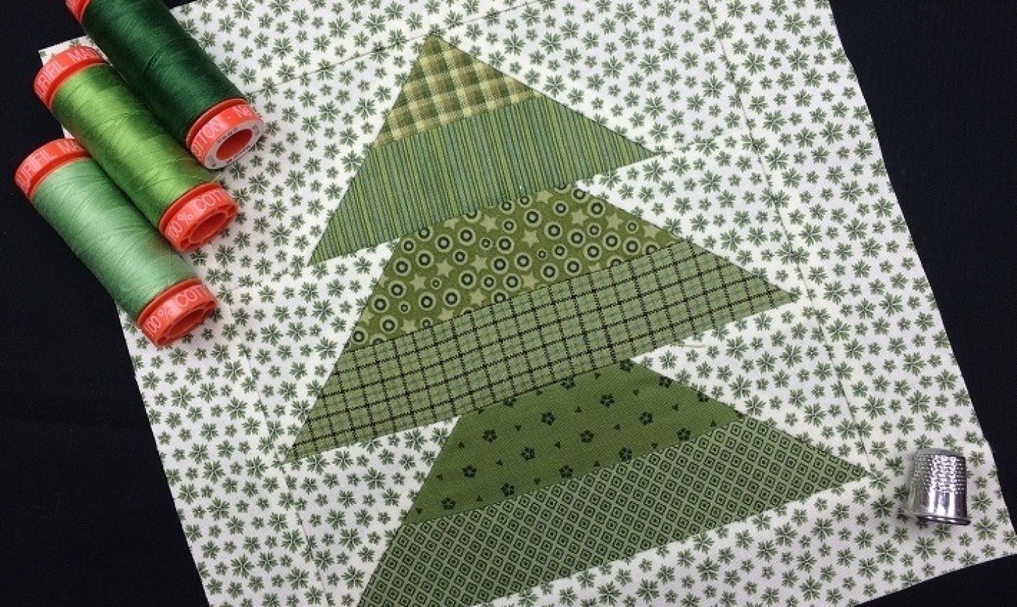 A Christmas tree quilt block in all green with some green thread on the left side