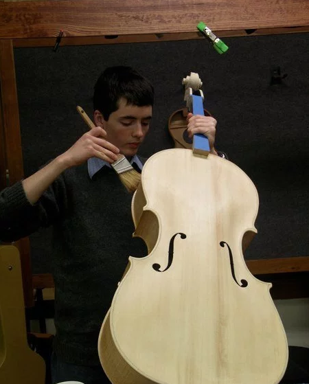 person staining a wooden cello