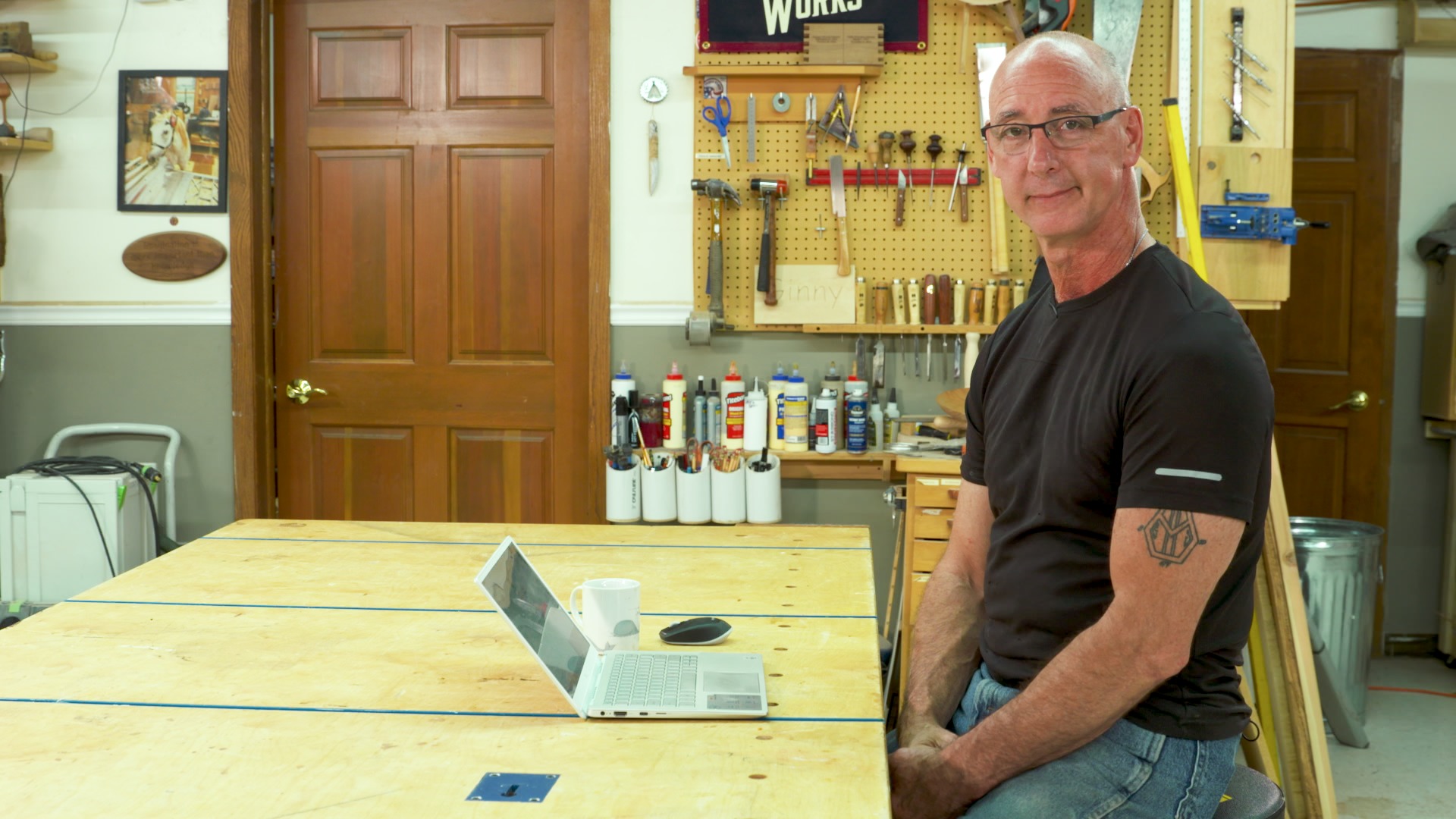 man sitting at a woodworking table with an open laptop