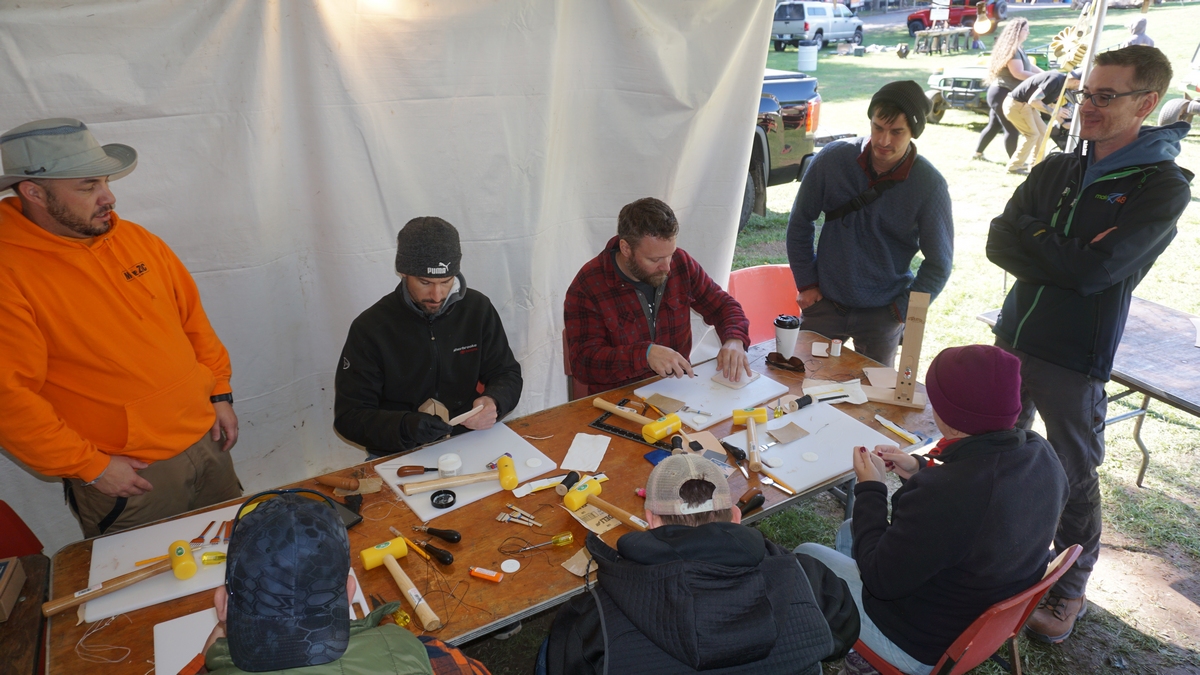 men sitting at an outdoor table in a tent practicing leatherwork
